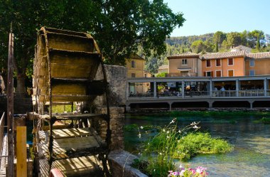 Fontaine de Vaucluse, Provence, Fransa. 09 Ağustos 2022. Eski ahşap su çarkı. Sorgue Nehri. Turistler arka plandaki restoranlarda yemek yiyorlar. Ünlü bir yer..