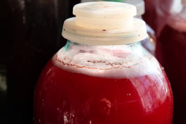 Kırmızı şarabın fermantasyonu. Cam kavanoz. Şarap fermantasyonu için hava kilitleri olan plastik kapaklı. Bardaktaki fotoğrafçının yansıması..