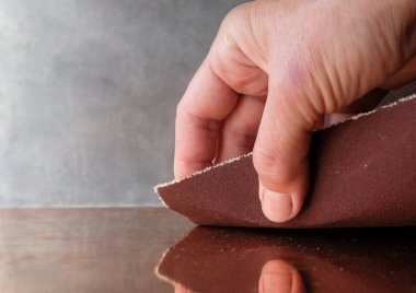 Metal zemin üzerinde zımpara kağıdı olan insan eli. Zımpara. Zımpara kağıdının tanecikliği.