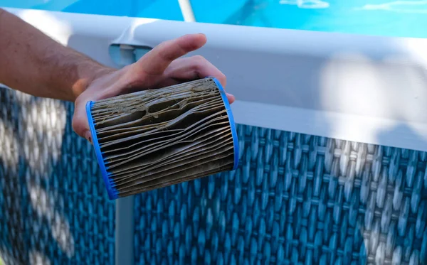 Dirty Replacement Pool Filter Cartridge in a man\'s hand. Pool background.