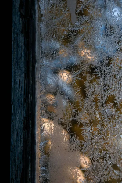 Old wooden window. Frost patterns on the window glass. Snowy spruce.