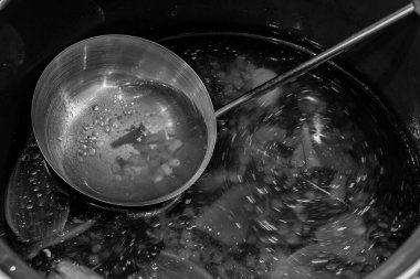 Stainless soup ladle is in the soup. Broth movement. Fat. Black and white.
