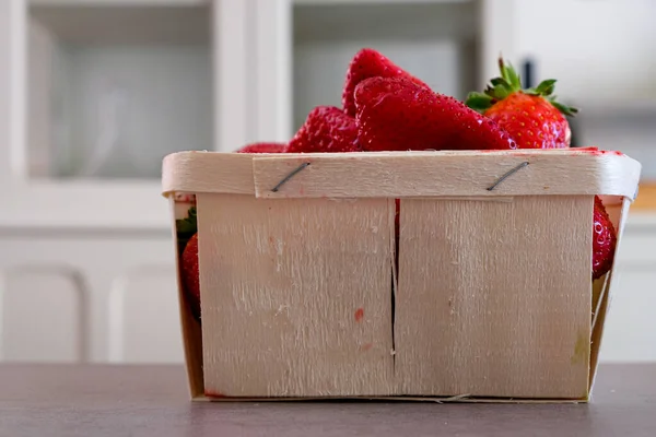 Strawberries in a wooden food package box on a kitchen background. Copy space.