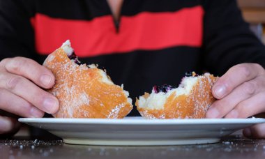 Adam donut ya da ponchik yiyor. Yabanmersinli geleneksel çörek. Şeker tozu. Yerel küçük gıda işi. Svitiaz Gölü, Shatsk Ulusal Doğal Parkı, Ukrayna.