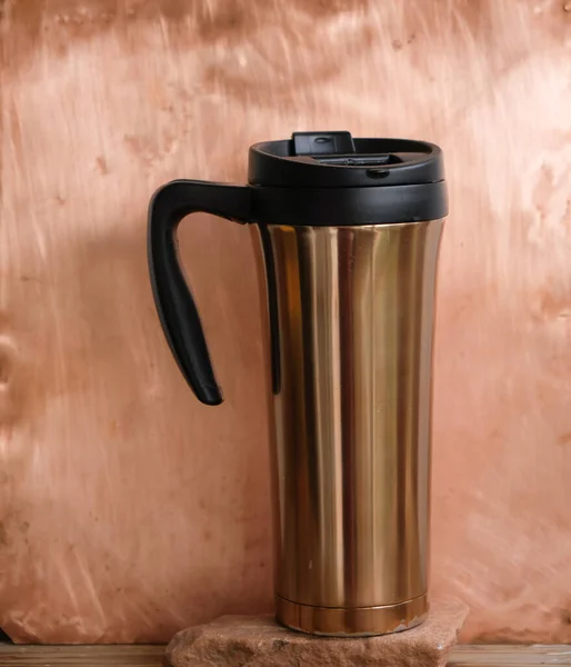 The thermos cup or travel mug of the copper color. Copper wall.
