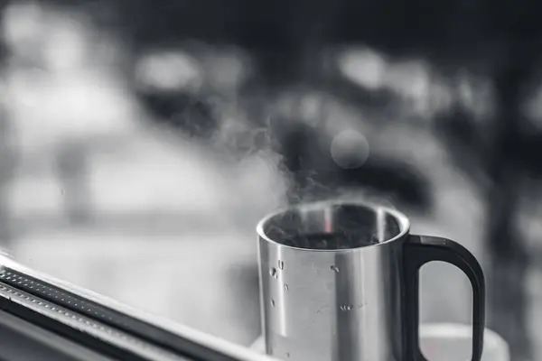 Metal cup. Steam. Window. Mood photo. Blurred background. Black and white. Copy space.