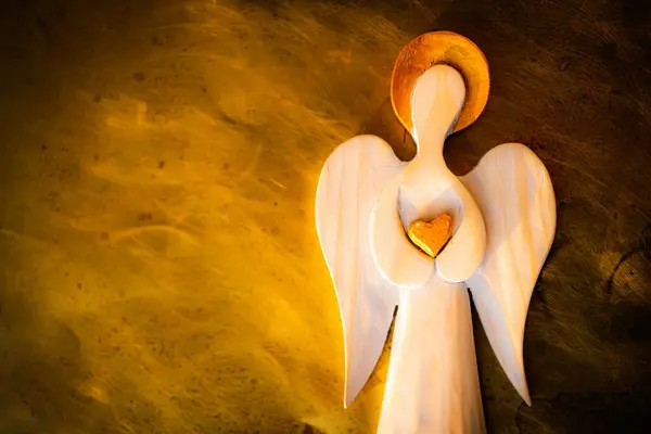 Altın haleli tahta bir melek figürü. Altın kalp. Arka plan taklidi yakılıyor. Taneli fotoğraf.