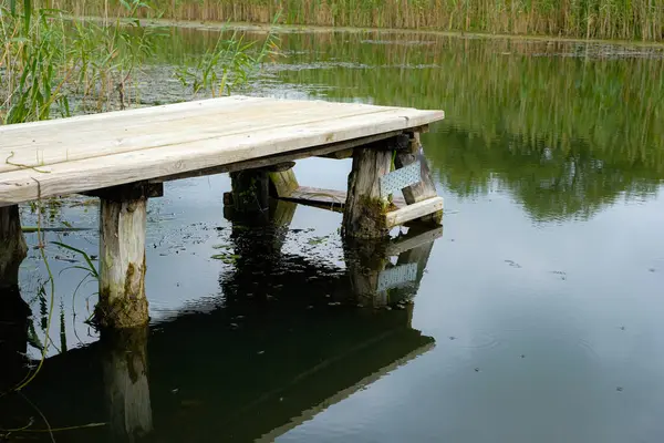 Eski el yapımı ahşap köprü. Nehir ya da göl kıyısında. Suya bir merdiven. Geleceğin Alacakaranlık Renk Suyu.