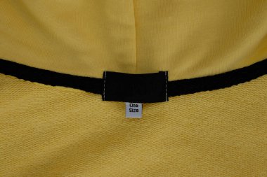 Sarı kapüşonlunun üzerinde bir beden kıyafet etiketi var. Kıyafet etiketi tasarımı. Tek beden hepsine uyar..