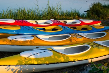 Colorful kayaks or canoes on a lake background. Entertaining water transport. Active recreation rental of watercraft. Morning sharp shadows. clipart