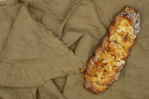 Meyveli bademli çörek. Karamelli elmalı ya da armutlu tatlı pasta. Badem serpiştirilmiş. Kahverengi keten kumaş. Uzayı kopyala Üst görünüm.