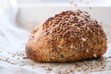 Ekşi hamurlu çoklu tahıllı ekmek. Kenevir kabuklu kumaş üzerinde ayçiçeği tohumlu ekşi ekmek. Tohumlar ekmeğin üzerine döküldü. Uzayı kopyala Sığ alan derinliği.