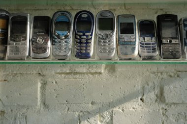 February 26, 2025. Lutsk. Volyn region. Ukraine. Collection of old Siemens mobile phones on a transparent glass shelf. Old textured white brick wall. clipart