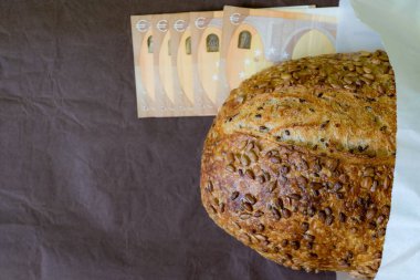 Kağıt ambalajında çoklu tahıllı ekmek ve kahverengi arka planda Avrupa Birliği parası. Ekmek odağı. Üst Manzara. Boşluğu kopyala.