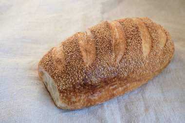 Kenevir masa örtüsü üzerinde susamlı beyaz ekmek. Susamlı ekmekler serpiştirilmiş. Yumuşak güneş ışığı. Boşluğu kopyala.