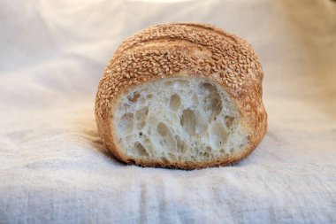 Kenevir masa örtüsünde dilimlenmiş susamlı beyaz ekmek. Susam tohumları serpiştirilmiş ekşi ekmek. Yumuşak güneş ışığı. Boşluğu kopyala.