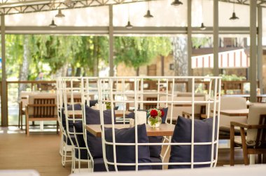 Açık hava yaz restoran terası, beyaz metal ve ahşap mobilyalar, kanepe yastıkları, çiçekler, gölgelik, güneş koruması