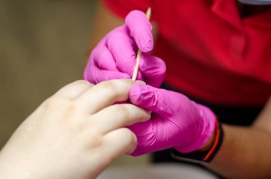 Pembe eldivenli kadın manikürcü genç elleri ve tırnaklarıyla parlak bir lambanın altında çalışır. Kayısı çubuğuyla tırnak derisini kaldırma işlemi