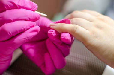 Pembe eldivenli kadın manikürcü genç elleri ve tırnaklarıyla parlak bir lambanın altında çalışır. Kayısı çubuğuyla tırnak derisini kaldırma işlemi