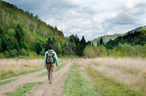 緑のジャケットで孤独な若い男のハイカー 暗い髪とバックパック付き 木と山の中を歩く 景色を楽しむ — ストック写真
