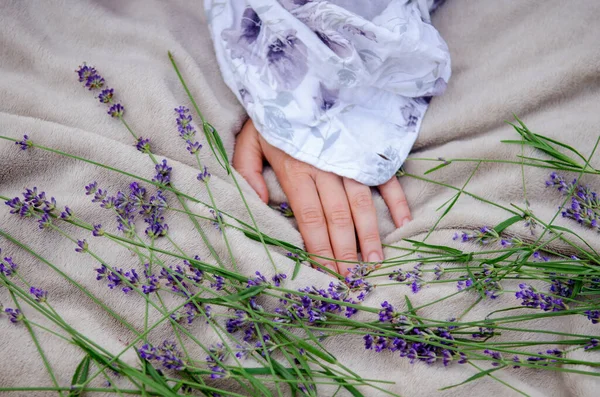 stock image Woman hand in a delicate shirt lies on a soft gray blanket in the garden with sprigs of lavender on a picnic