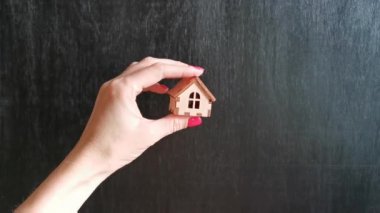 Kadın eli, siyah arka planda ahşap bir ev gösterir, konut, ev, apartman, daire seçimi kavramı.