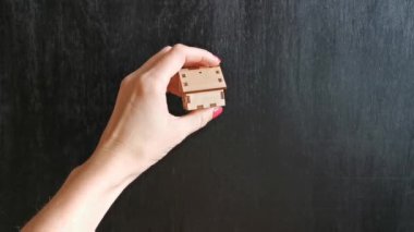 Kadın eli, siyah arka planda ahşap bir ev gösterir, konut, ev, apartman, daire seçimi kavramı.