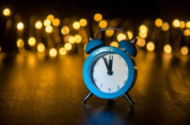 Classic arrow blue alarm clock on a black background, illuminated from the side, behind round yellow blurred lights