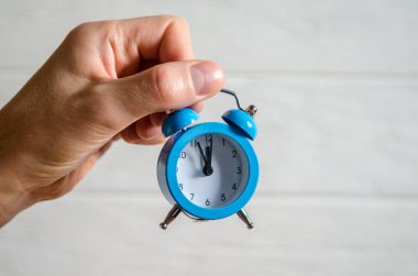 Classic arrow blue alarm clock on a man hand on a white background, concept of the passage of time