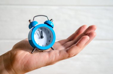 Classic arrow blue alarm clock on a man hand on a white background, concept of the passage of time