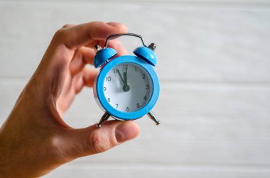 Classic arrow blue alarm clock on a man hand on a white background, concept of the passage of time