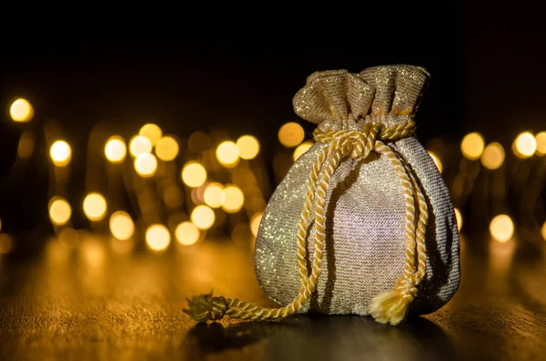 Small golden gift bag on a black background illuminated by light from side, round yellow blurred lights behind