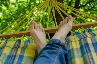 Çıplak kadın bacakları, kot giymiş, kareli bir hamakta, ormandaki açık hava eğlencesi, yeşillikler arasında.