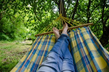 Çıplak kadın bacakları, kot giymiş, kareli bir hamakta, ormandaki açık hava eğlencesi, yeşillikler arasında.