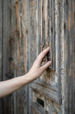 Genç kadın eli ve parmakları çok eski gri bir kapıya dokunuyor.