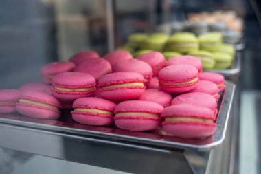 Buzdolabında cam vitrin, yansıma ve cam parlaklığı olan büyük miktarda pembe makaronlu tatlı kekleri görülebilir.