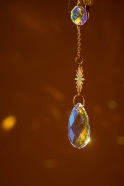 Metal altın zincirli cam güneş yakalayıcı, güneş ışığında parlıyor ve sarı arka planda gökkuşağını yansıtıyor.