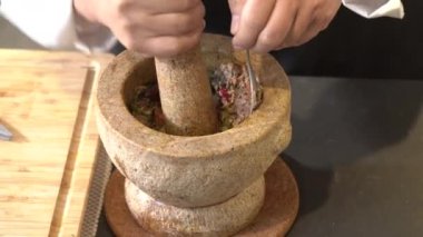 Şef kahverengi taştan havan topuna baharatlı karides ezmesi atıyor..