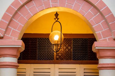 Pembe kemerin arkasındaki beyaz katlanır ahşap kapılar ve girişteki asılmış klasik lamba. Kapı kilitli..