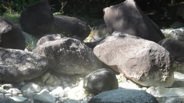 Gerçek doğada dağ kaplıcaları. Güneş altında bol miktarda kaya ve buharlı su var..