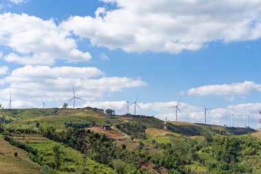 Güneşli bir günde, beyaz bulutlar ve mavi gökyüzünün altındaki çim tepesinin tepesindeki rüzgar türbinleri saf enerjiden elektrik üretiyordu..