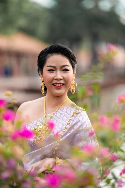 stock image A woman in a traditional Thai costumes is standing on the wooden bridge while being taken a portrait photo shooting.