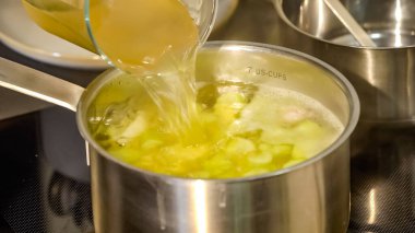 Şef, elektrik ocağındaki cızırdayan çelik tencereye ustalıkla biraz su katar. İçindeki köpüren çorbadan buhar fışkırmasına neden olur..