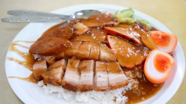 Bir tabak kızarmış kırmızı domuz eti, çıtır çıtır domuz eti ve buharda pişmiş beyaz pirinç yatağının üzerinde mükemmel bir şekilde kaynamış yumurta ile kıtır kıtır domuz eti ve zengin sarısı karışımı.