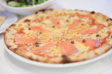 Somon füme ile nefis sıcak pizza, ahşap masada yemeye hazır. Somon ve mozzarella ile tütsülenmiş somon pizzası. Bulanık yeşil salata arka planında füme somon pizzası..