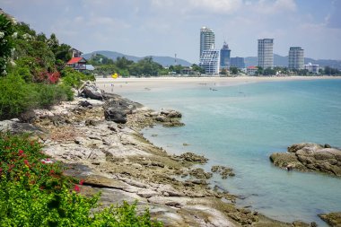 Hua Hin, Tayland 'daki sakin sahil manzarası, ufukta gökdelen manzarası ve mavi gökyüzü. Plaj kayaları ve tropikal bitkiler.