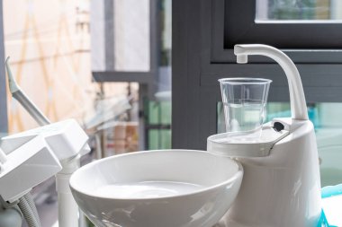 Modern seramik ağız temizleyicisinin bir bardak tutacağında plastik bir bardak. Bir pencerenin yakınındaki dişçi ofisinde lavabo., 