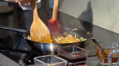 Bir aşçı elektrikli sobada spatulası olan tavada Pad Thai eriştesi kızartır. Geleneksel Pad Thai yemeği için sos tabakları.