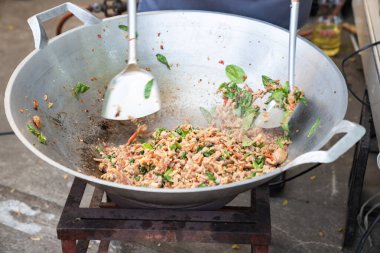 Domuzlu Tayland geleneksel Fesleğenini deneyin. Manzaralı bir alanda pişmiş büyük bir tavada canlanıyor. Çevirici bir dokunuşun uzman dokunuşuyla..