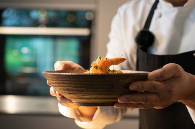 Şefin eli, pişmiş karidesi fırının arka planında bulanık bir şekilde kasede tutuyor..